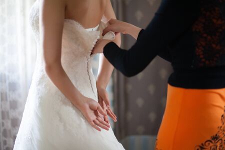 Bride from the back. Bridesmaid zips the wedding dress.