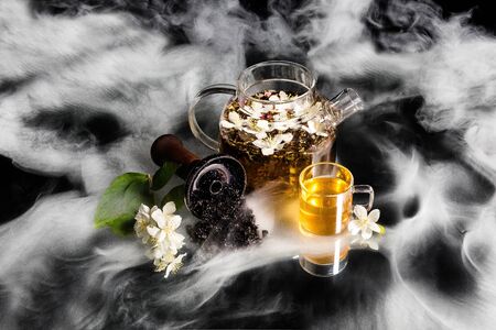 Hookah bowl with tobacco in the smoke. Jasmine shisha tobacco. Glass teapot and jasmine cup.