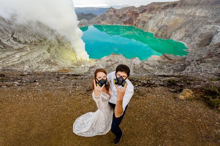 The bride and groom in respirators show sign of the horns against the background of a green lake and...