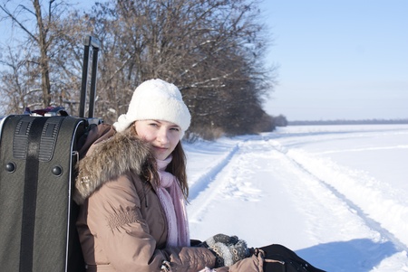 Teen girl with a suitcase outdoors at winter timeの写真素材