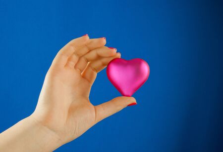 Hand holds a heart shaped gift against blue backgroundの写真素材