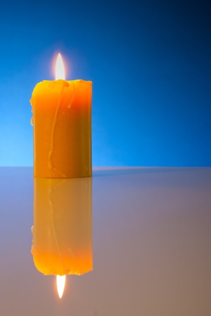Burning yellow candle against blue backgroundの写真素材