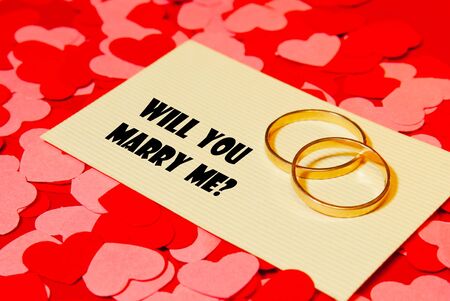 Two rings and a card with marriage proposal on the red backgroundの写真素材