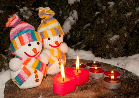 Two snowmen with two burning heart shaped candles staying outdoorsの写真素材