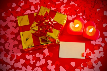 Presents and two heart shaped candles with blank card on red background