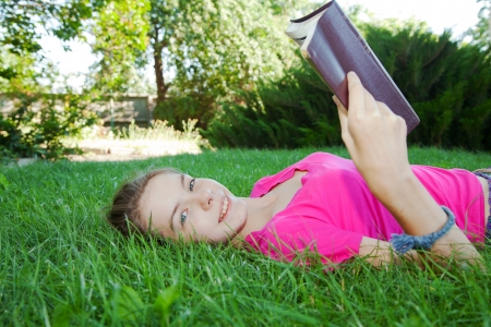 Teen girl reading the Bible outdoors lying on the grassの写真素材