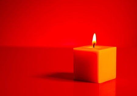 Burning yellow candle over the red backgroundの写真素材