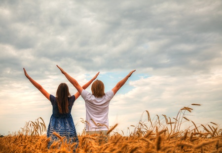 Couple staying with raised hands at a wheat field at sunset timeの写真素材