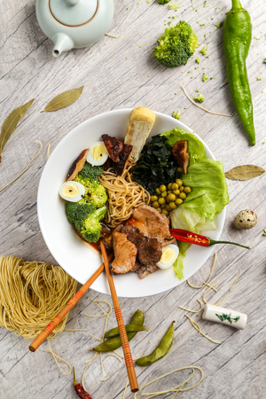 Traditional Japanese cuisine, soup with noodles, vegetables and seafood in a white plate on a wooden background, view from the topの写真素材