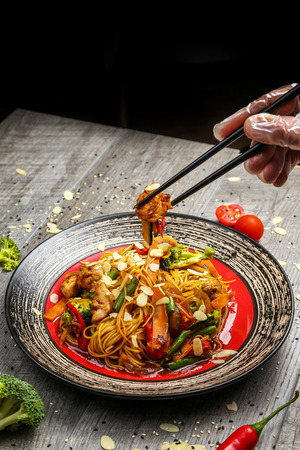 Traditional Japanese cuisine, noodles with chicken and vegetables on a black plate with chopsticksの写真素材