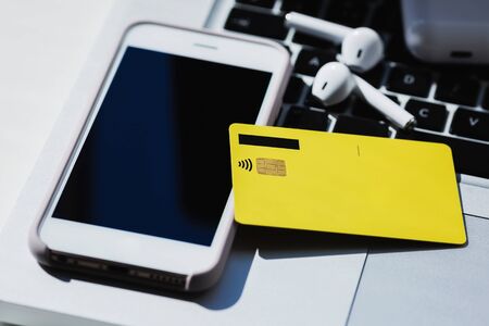 yellow credit card, smartphone screen, laptop keyboard and earphones.