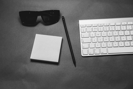 Black and white office desk table with keyboard, notepad, pen and glasses.の写真素材