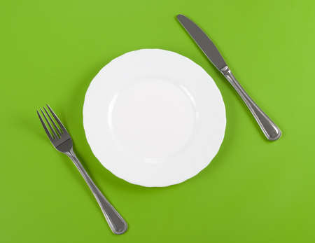 Knife, white round plate and fork on green background