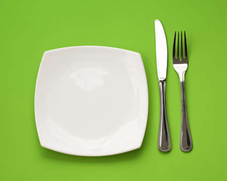 Knife, square white plate and fork on green backgroundの写真素材