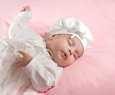 Little 3months baby-girl sleeping on pink sheet dressed in white suitの写真素材