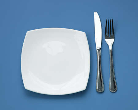 Knife, square white plate and fork on blue backgroundの写真素材