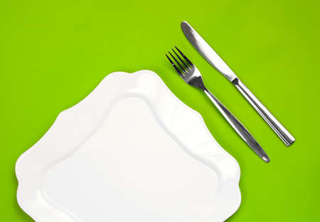 Knife, figured white plate and fork on green backgroundの写真素材