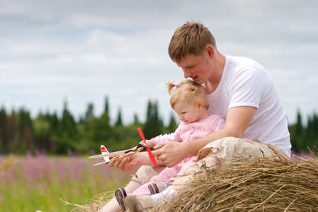 Father and daughter have fun with toy aircraft model on haystackの写真素材
