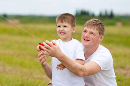 Father and son fly a kite together in summer fieldの写真素材