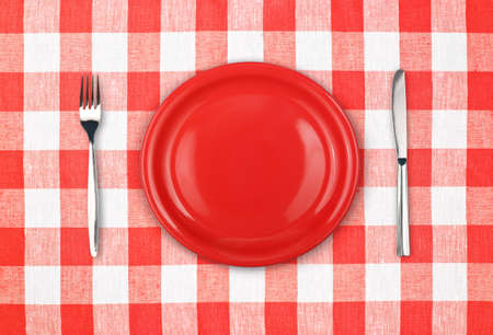 Knife, red plate and fork on checked tableclothの写真素材