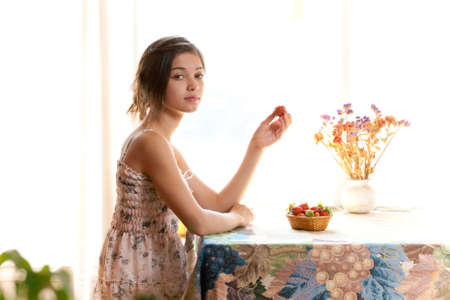 Girl eating strawberries sitting at table indoor in summer dayの写真素材