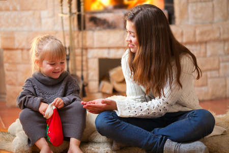 Two girls sitting fireside and opening christmas presentsの写真素材