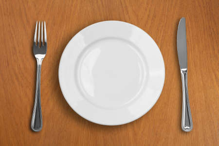 round white plate, knife and fork on wooden tableの写真素材