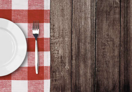 white plate and fork on old wooden table with red checked tablecloth and copyspaceの写真素材