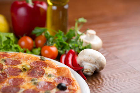 Salami pizza on table with vegetables and empty roomの写真素材