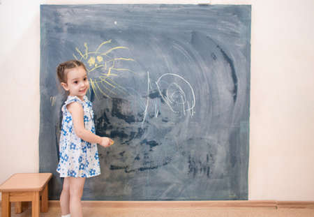 Full length cute kid girl standing near blackboardの写真素材