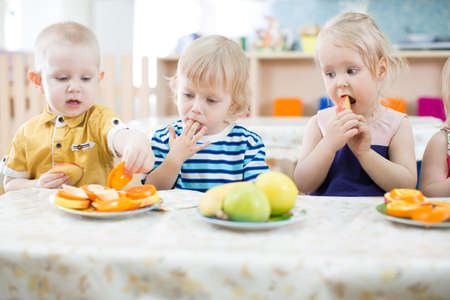 Three funny kids eating fruits in kindergartenの写真素材