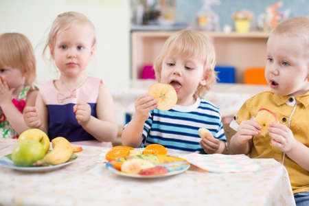 funny children group eating fruits in kindergarten dinning roomの写真素材