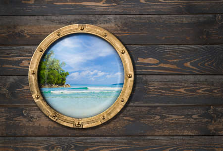 ship porthole on wooden wall with tropical island behindの写真素材