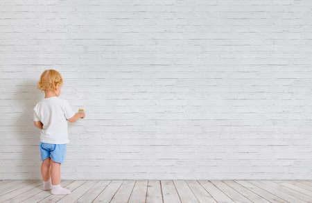 Baby boy with paint brush standing back near brick wallの写真素材