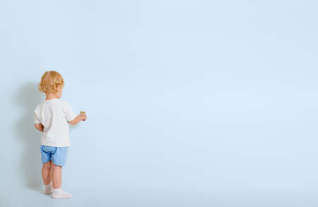 Little boy with paint brush standing back near blue wallの写真素材