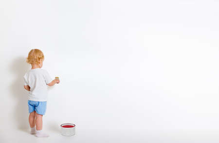 Little boy with paint brush and tin can standing back near white wallの写真素材