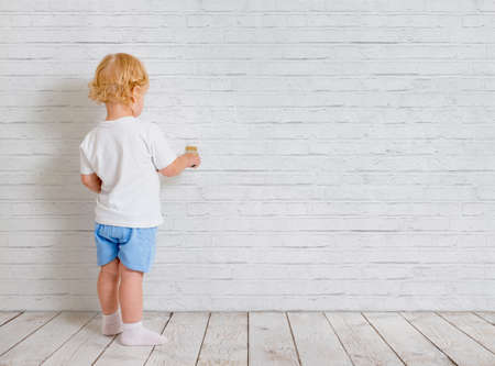 Baby boy with paint brush standing back near brick wallの写真素材