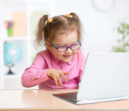 Happy kid in spectacles using notebook with great interest in schoolの写真素材
