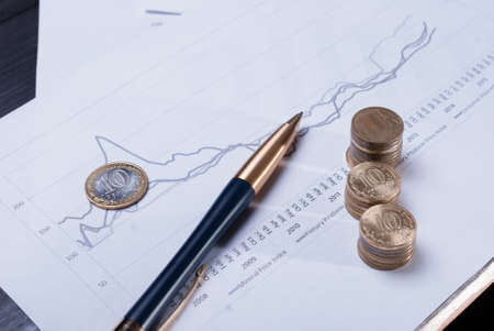 Pen and coins lying on financial charts. The business concept.