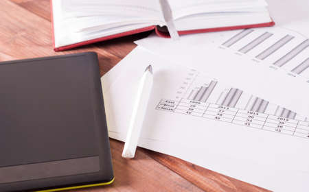 Tablet, notebook and pen lie on white business papers.