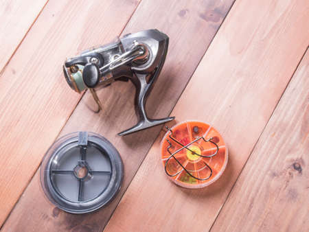 Fishing gear on wooden background. Silver coil, spools of fishing line, and yellow box for hooksの写真素材