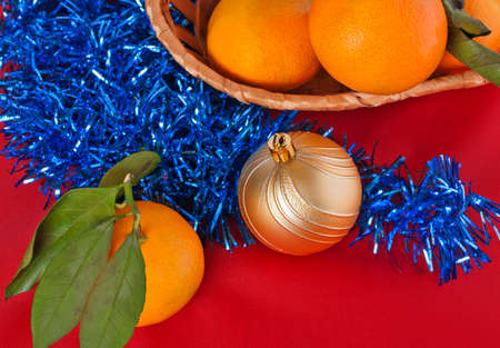 Yellow tangerines in the basket, Christmas ball and tinsel on a red backgroundの写真素材
