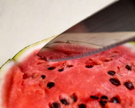 knife cutting a slice of watermelon with reflection on the knifeの写真素材