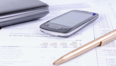 Business accessories - a pen, a phone and a laptop lying on tax documentsの写真素材