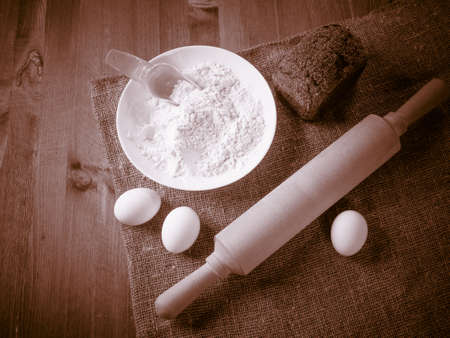Eggs, bread, flour and kitchen tools on a wooden boardの写真素材
