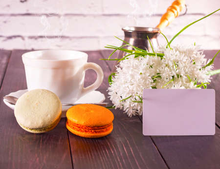 Cup of coffee, macarons on a plate and a bouquet of flowers. with a card the inscription の写真素材