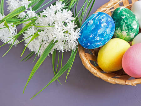 Basket with Easter eggs and bouquet of flowers on a gray background