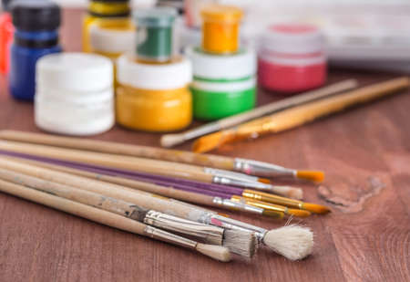 bunch of art used brushes and jars of paint on a wooden table