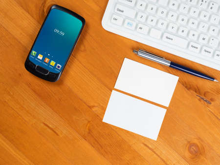 Top view on wooden table with white keyboard, smart phone with green screen and business cards