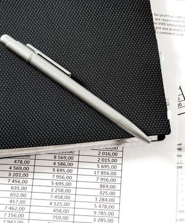 Silver pen on a black notepad on a table with financial tables and documentsの写真素材